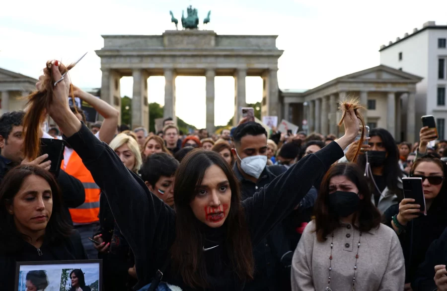 A demonstrator in Berlin, Germany holding her cut hair in front of a gathered crowd by Brandenburg Gate 